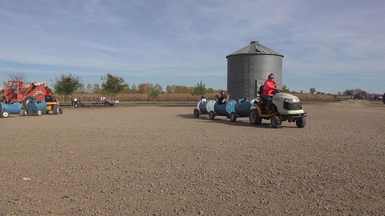 Tractor train enters a gravel farmyard near a silo.