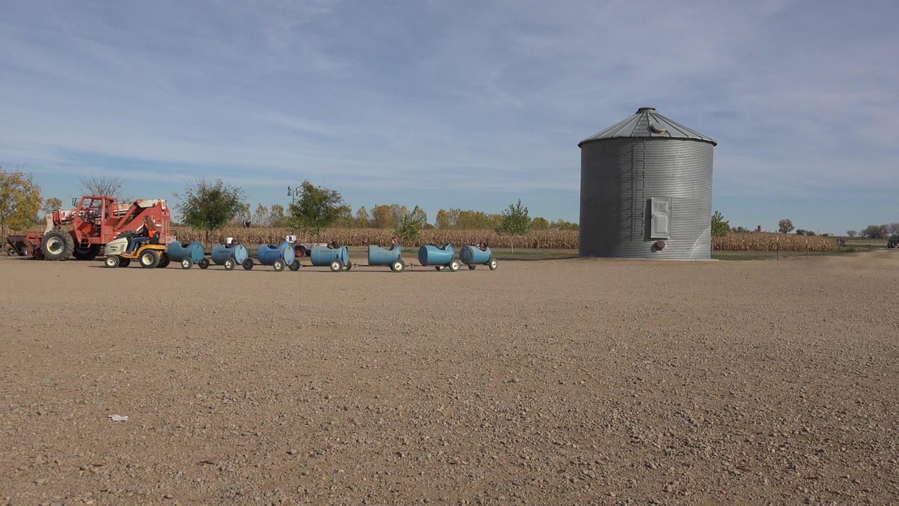 Brighton, Colorado farm-like setting with red equipment and blue wheeled carts or barrels spread across the midground beside a gray metal grain bin, with no visible people.