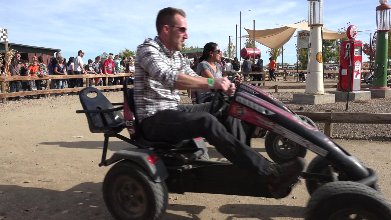 Close view of an adult riding a four-wheel pedal cart past the camera.