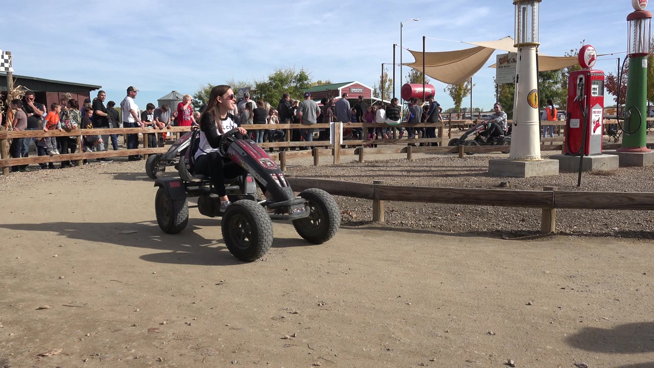 Woman rides a pedal kart past decorative pumps and spectators.