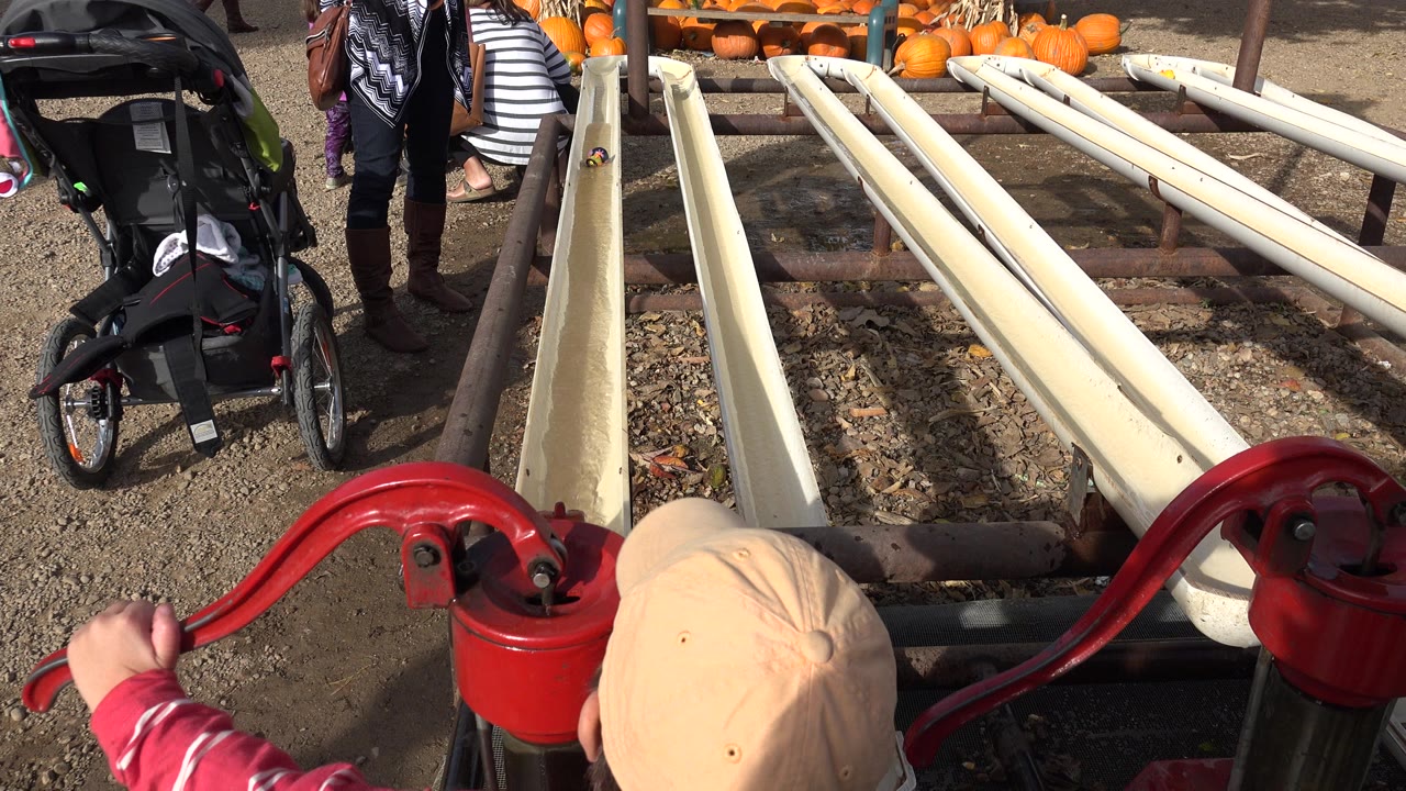 Child beside red hand-pump handles and pale irrigation tubes at a pumpkin patch.