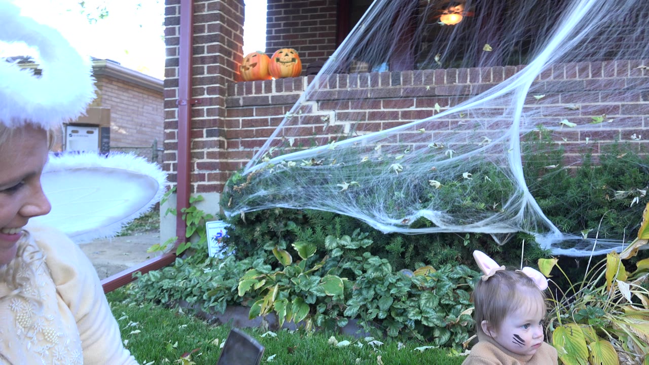 Woman in angel wings and child in costume beside Halloween porch decorations.
