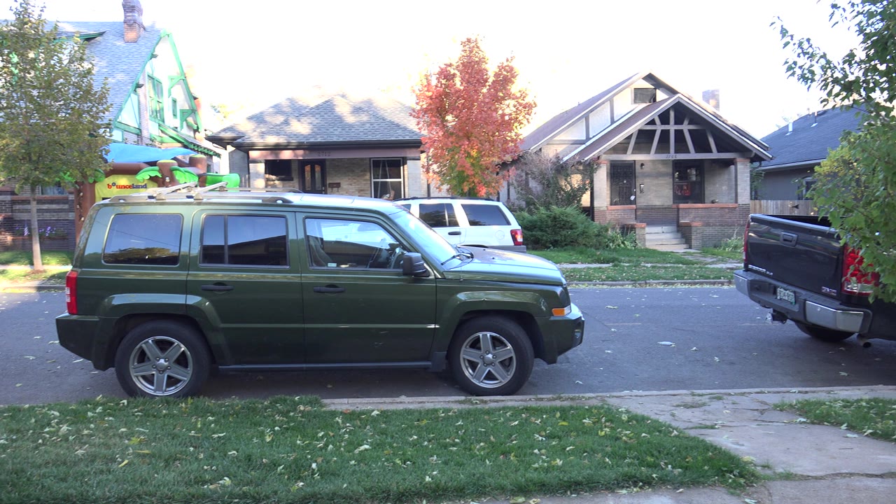 Green SUV parked on a suburban street in front of houses and trees.