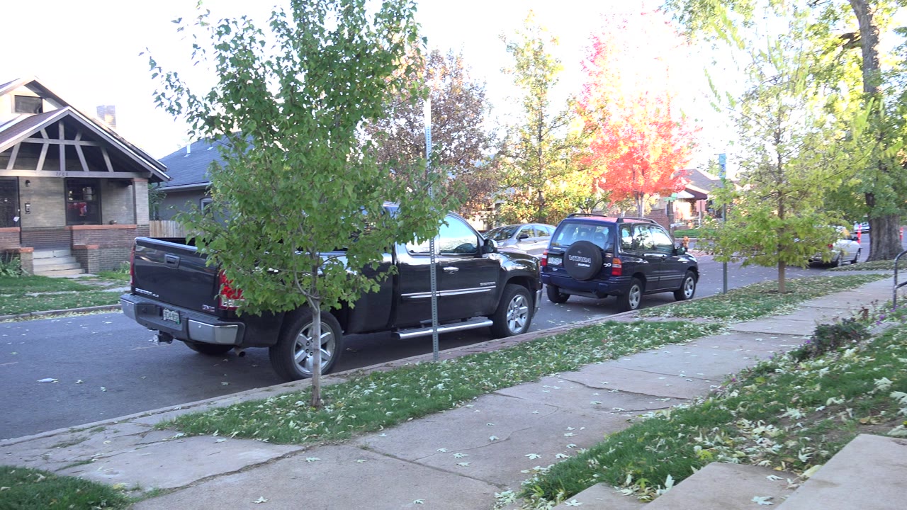 A Westminster, Colorado residential street with a black pickup, a dark SUV, sidewalks, lawns, autumn trees, and no visible people at the start of the clip.