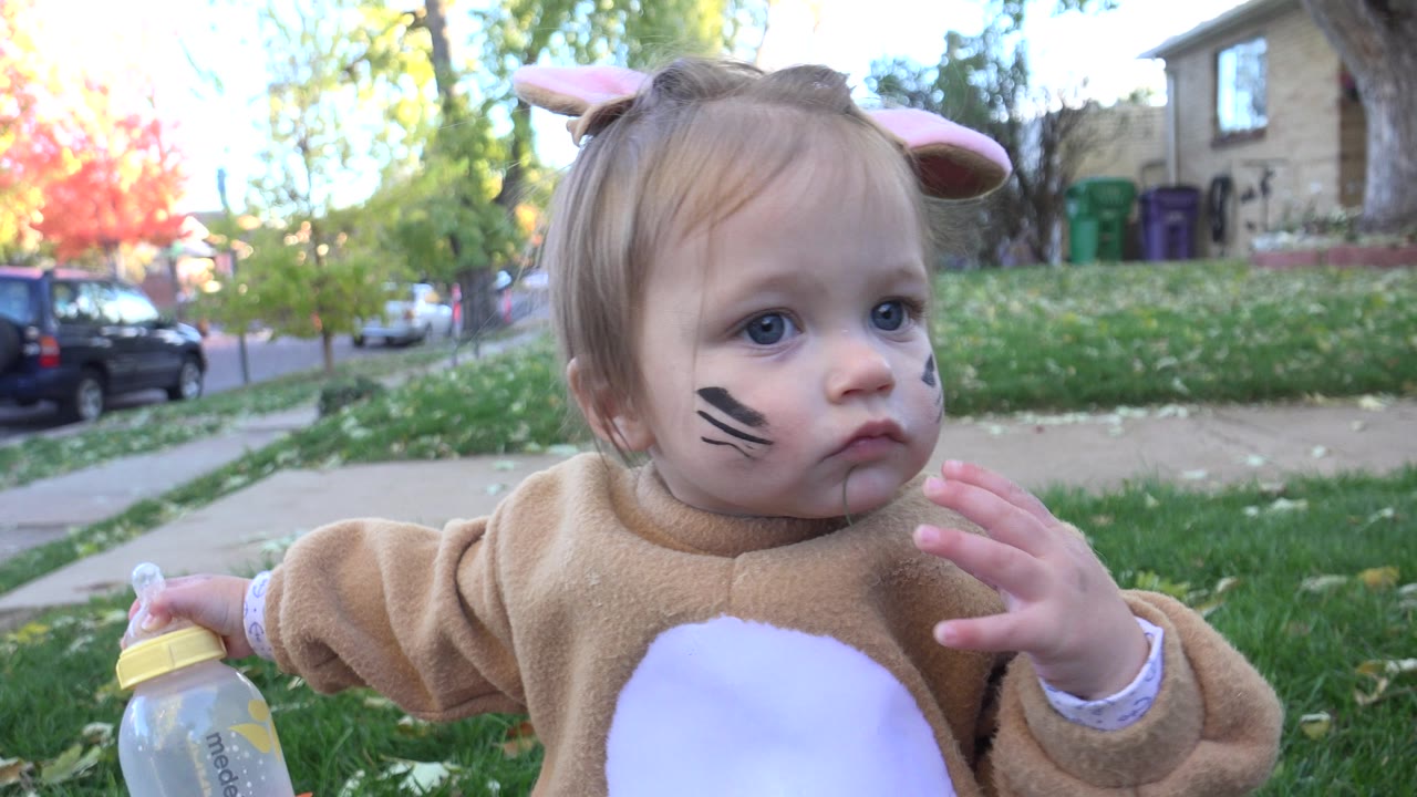 Baby in rabbit costume raises a hand near their face.