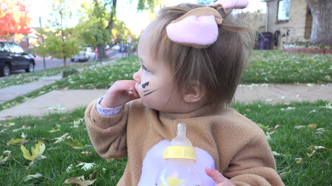 Toddler in costume holding bottle and looking toward the street.