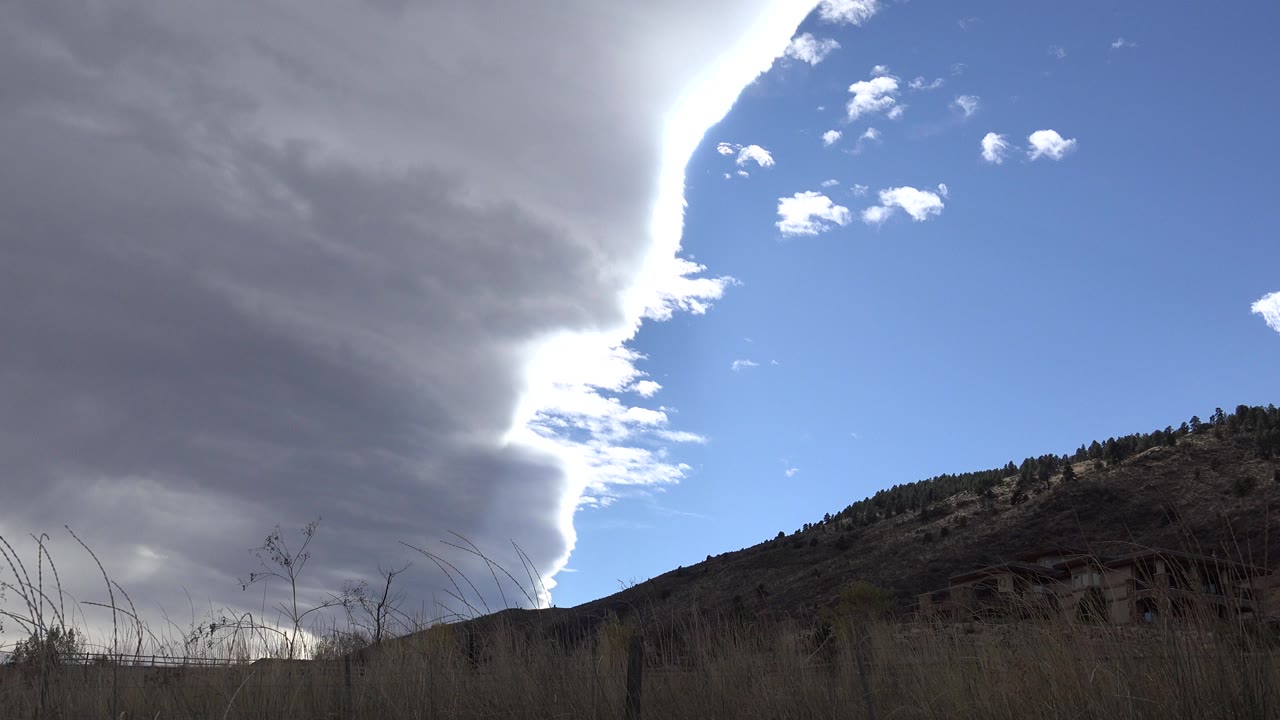 Gray cloud edge over blue sky and foothill grasses