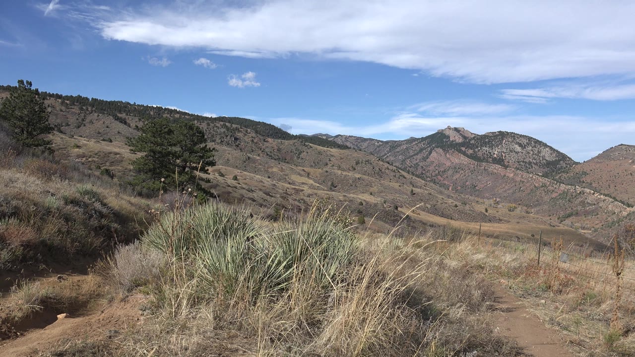 Open mountain basin with dry plants and cloud bands.