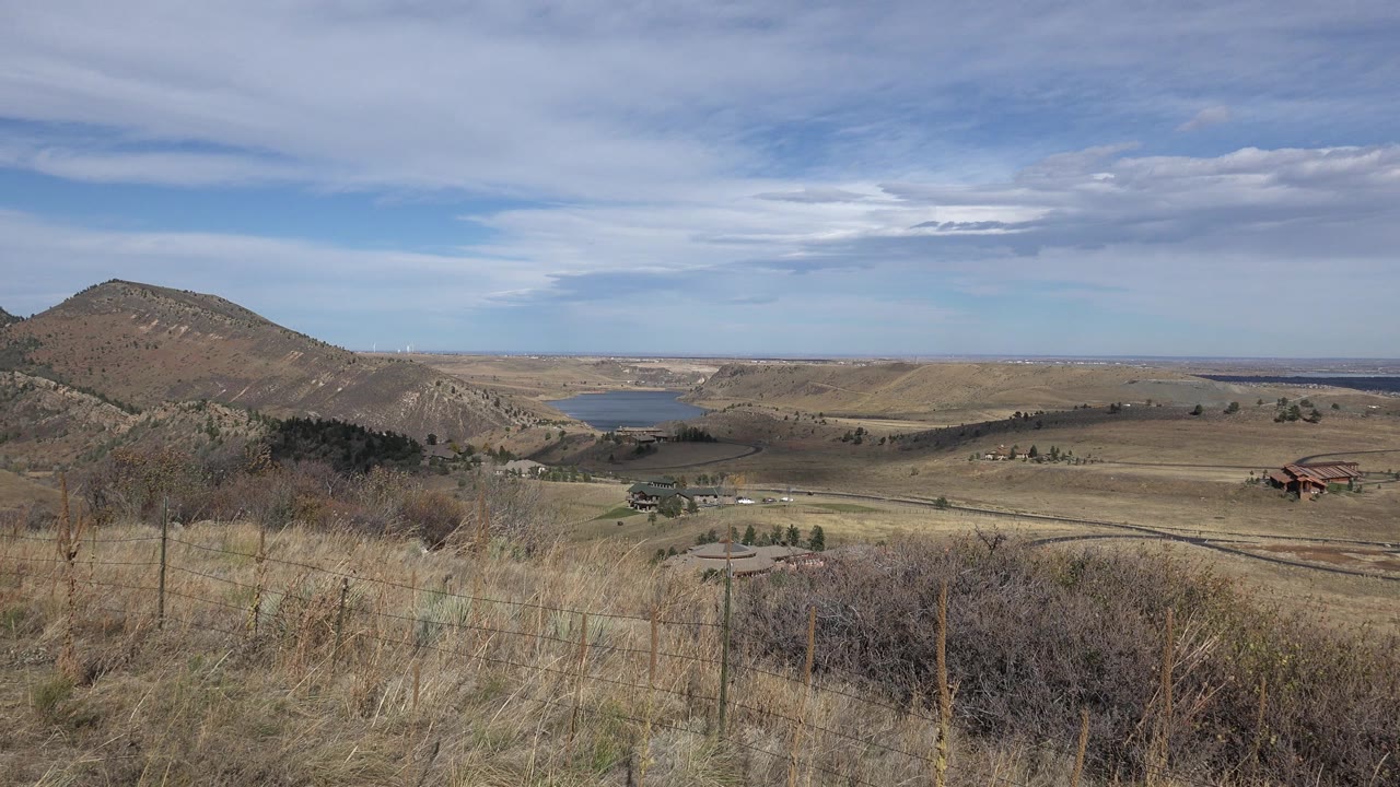 Wide dry grassland with hills, distant water, and cloudy blue sky.