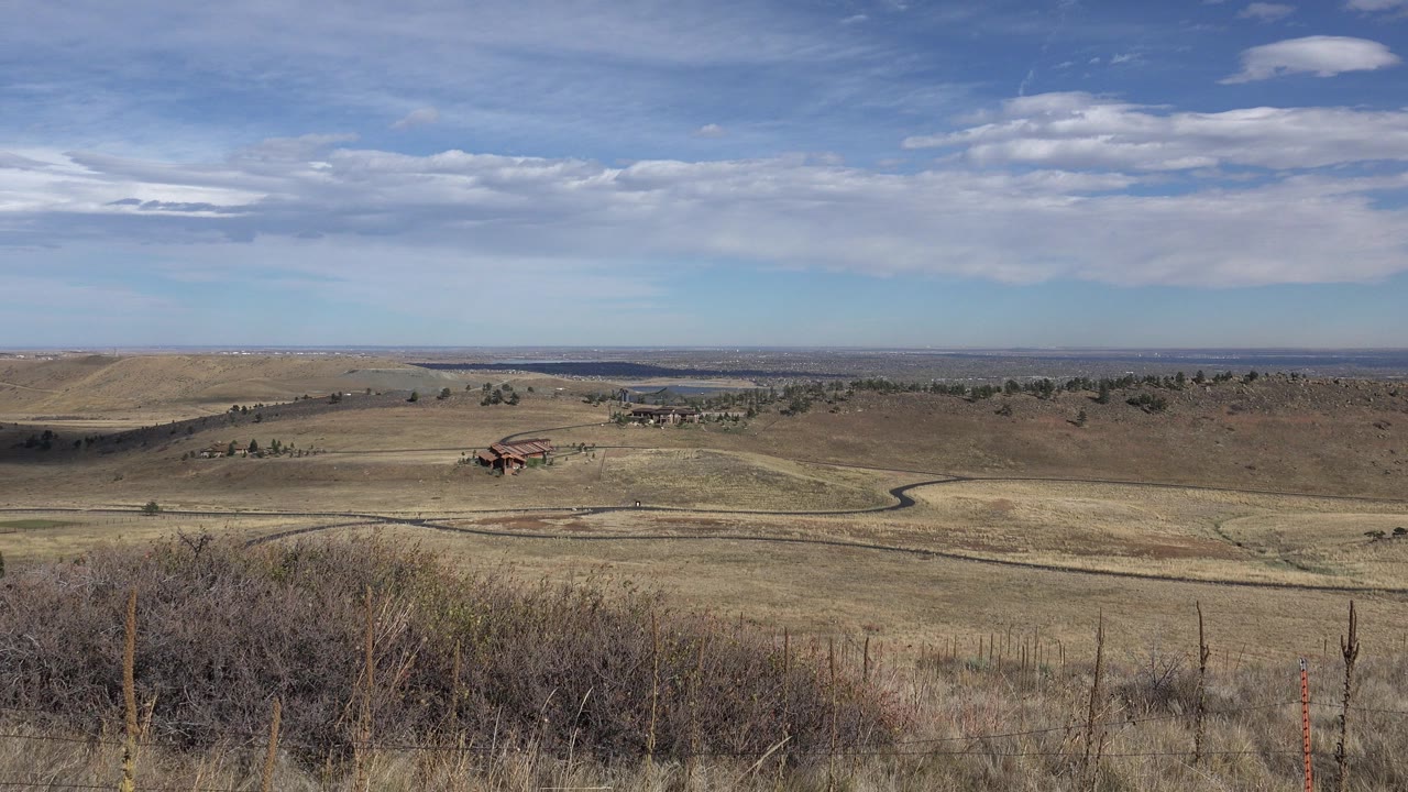 Dry hillside grassland overlooking a broad valley and cloudy sky.