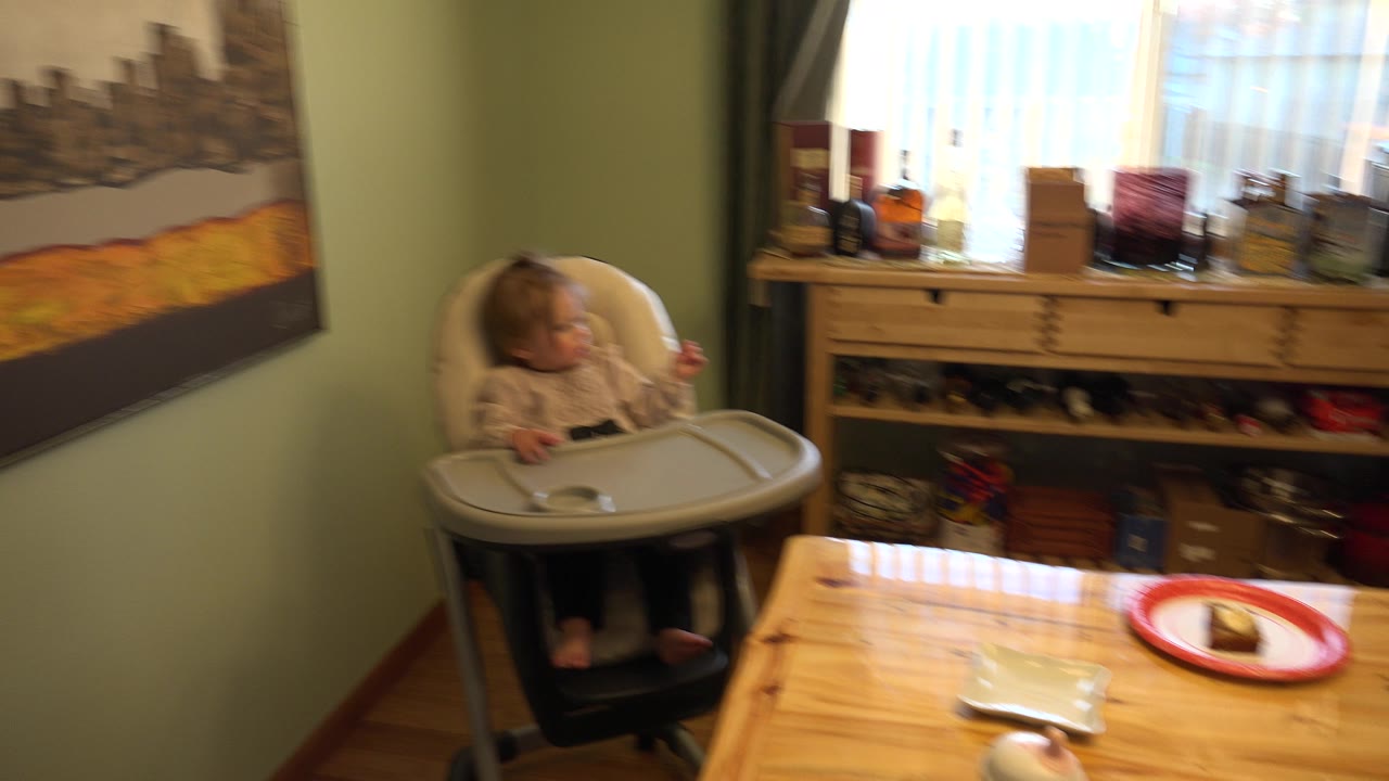 Baby in a high chair beside a wooden dining table in a home interior.