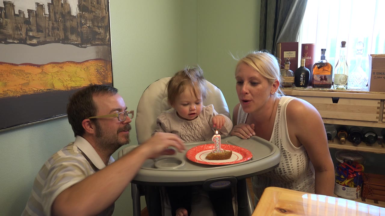 Parents beside a toddler in a high chair with a first birthday cake.
