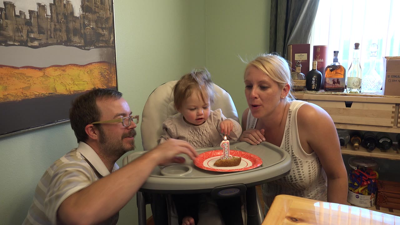 The Westminster, Colorado birthday scene shows the toddler focused on the cake while the adults stay close on either side of the high chair.