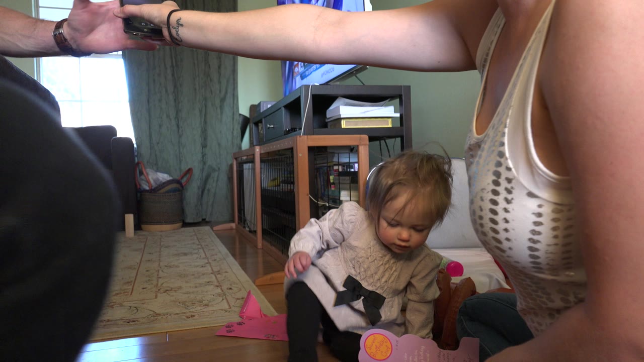 Woman reaches across a living room while a blonde baby sits on the floor.