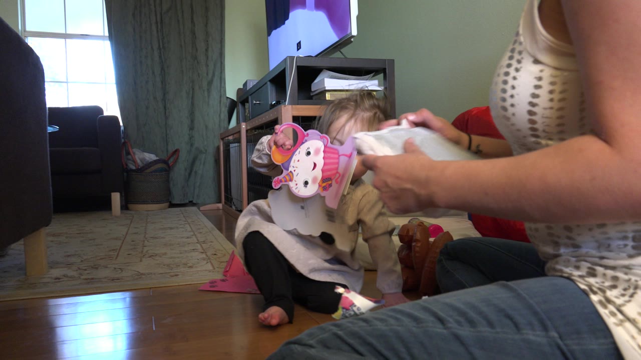 Baby sits on a living room floor while an adult opens fabric nearby.