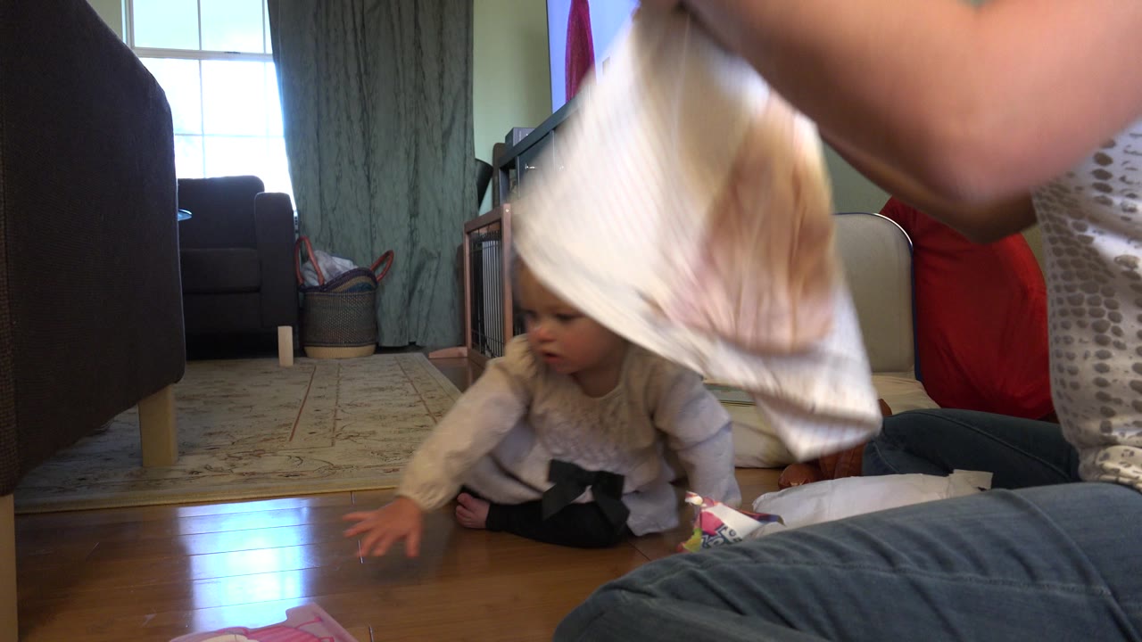 Baby on hardwood floor while clothing hangs close to the camera.