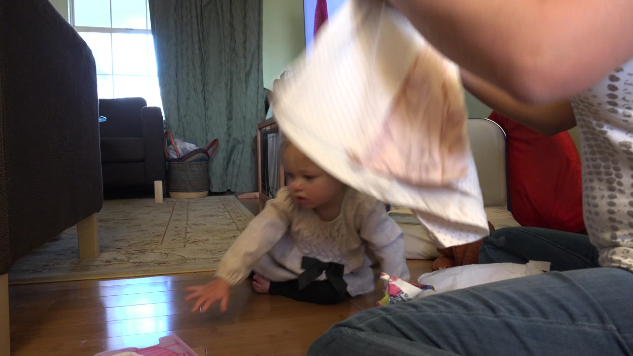 The baby leans forward on the hardwood floor while a white piece of clothing fills the foreground in a Westminster, Colorado home interior.