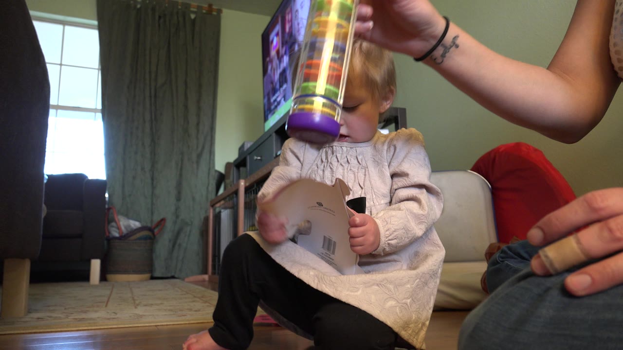 The Westminster home scene continues with the baby looking down at a card as the adult holds the bright tube toy just in front of the child.