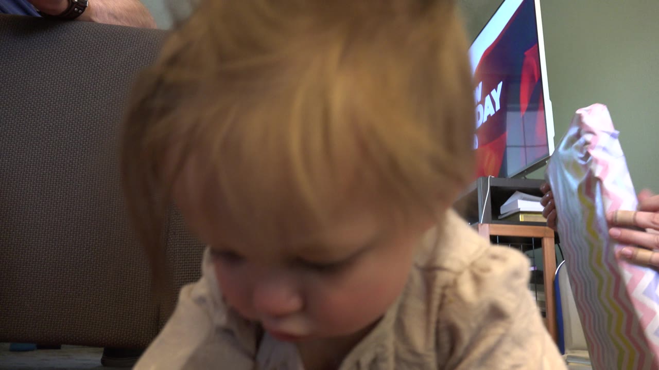 Toddler is close to camera with a pastel card and TV behind.