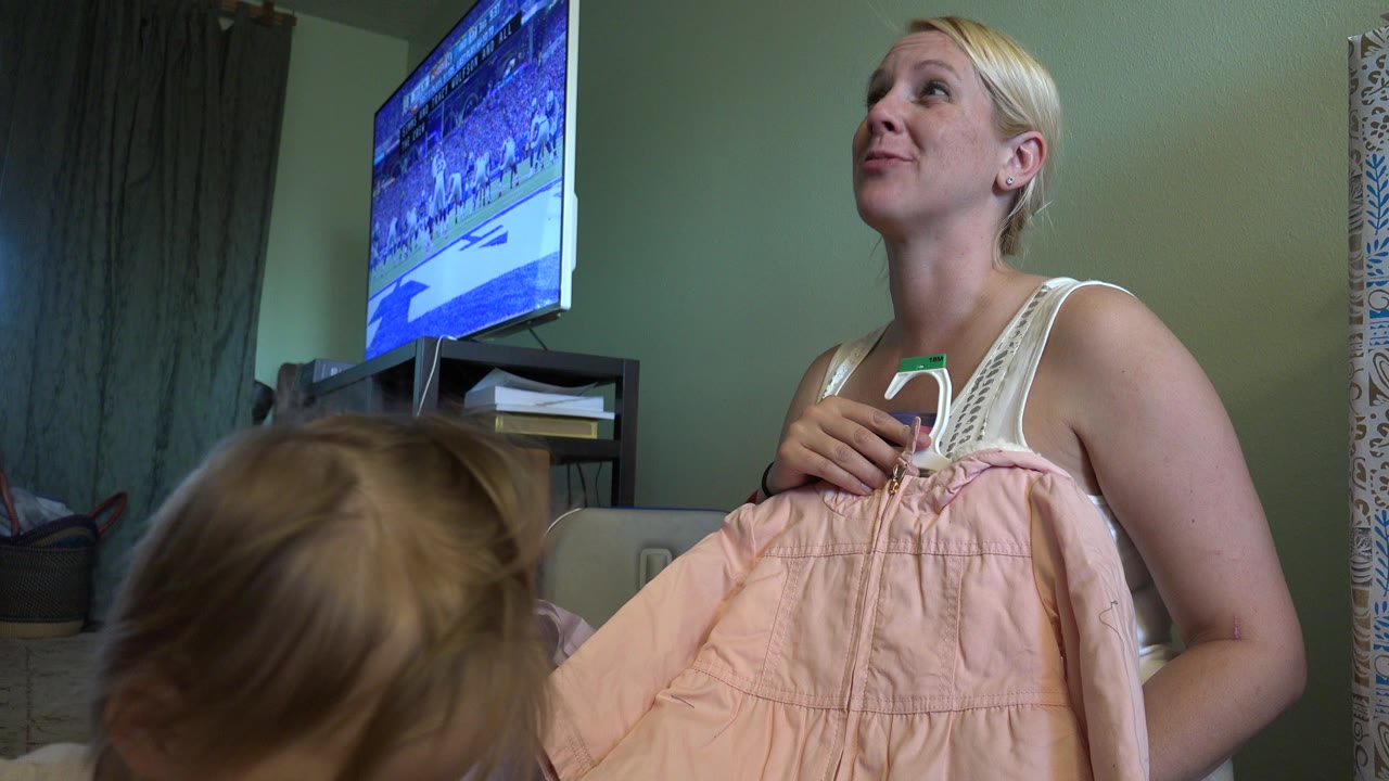 Woman holding a pink child's dress while a toddler is in the foreground.