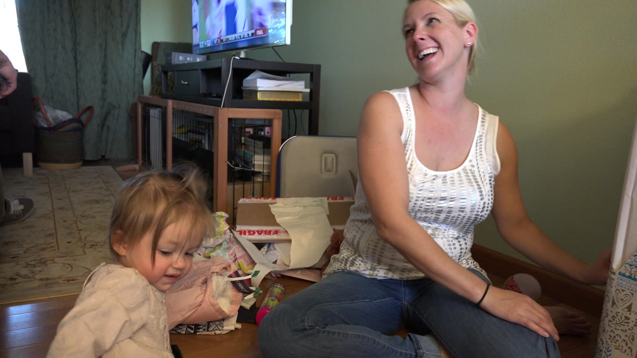 Laughing woman seated beside young child in a living room.