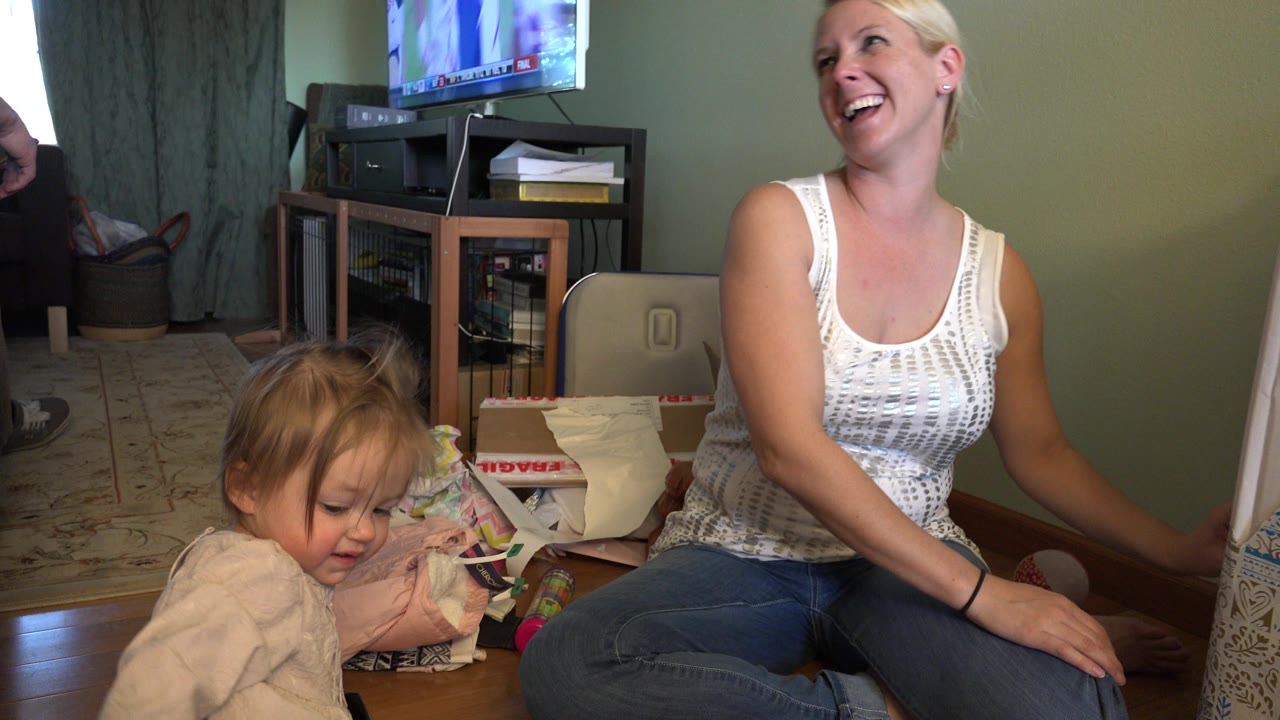 The mother smiles upward while the young girl looks down near paper and boxes in the Westminster, Colorado home interior.