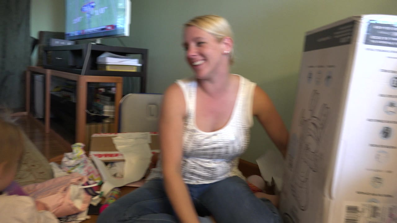 Smiling woman sits next to a toddler with a tall box in the foreground.