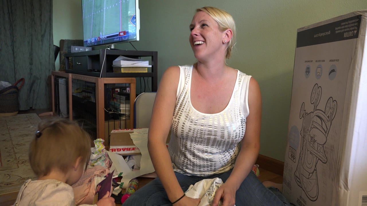 Mother laughing beside toddler and presents on living room floor.