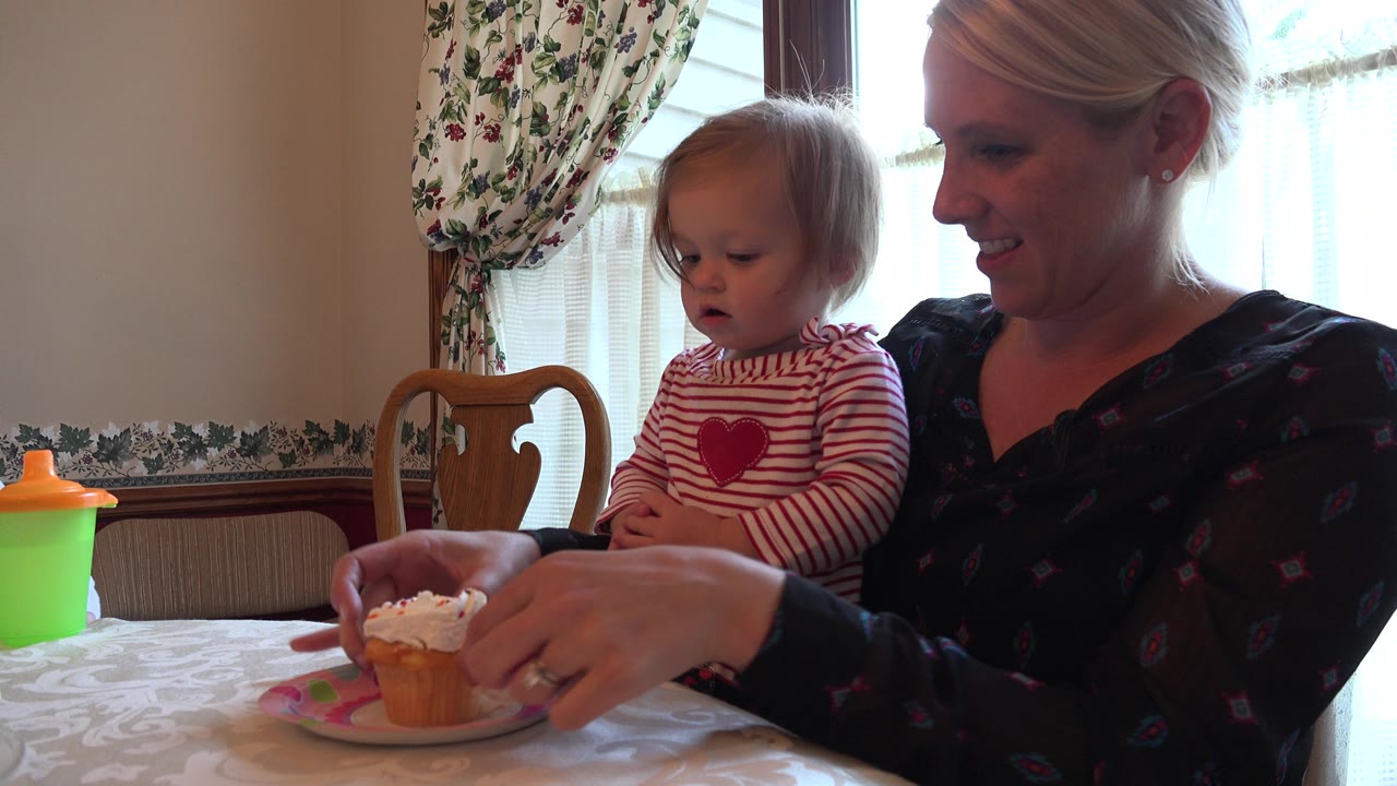In Prairie Grove, Illinois, a mother smiles beside a toddler in a striped shirt as a frosted cupcake sits on a small plate in front of them.