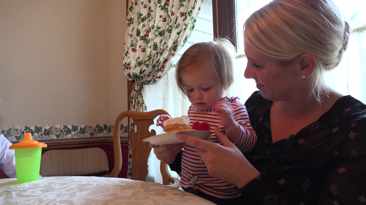 Toddler and woman hold a cupcake plate at a dining table.