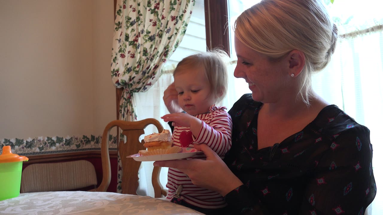In Prairie Grove, Illinois, the toddler points toward the cupcake as the mother smiles and holds the plate in the softly backlit dining room.