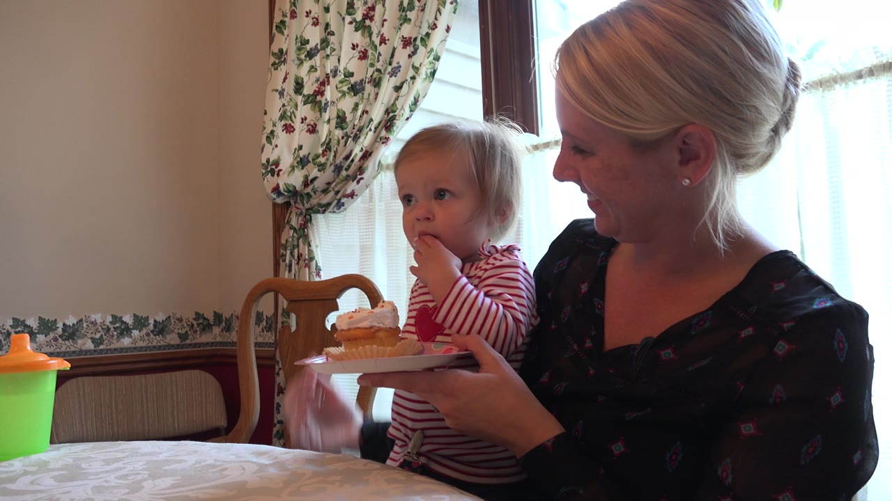 Toddler has a finger near the mouth while mother holds a cupcake plate.