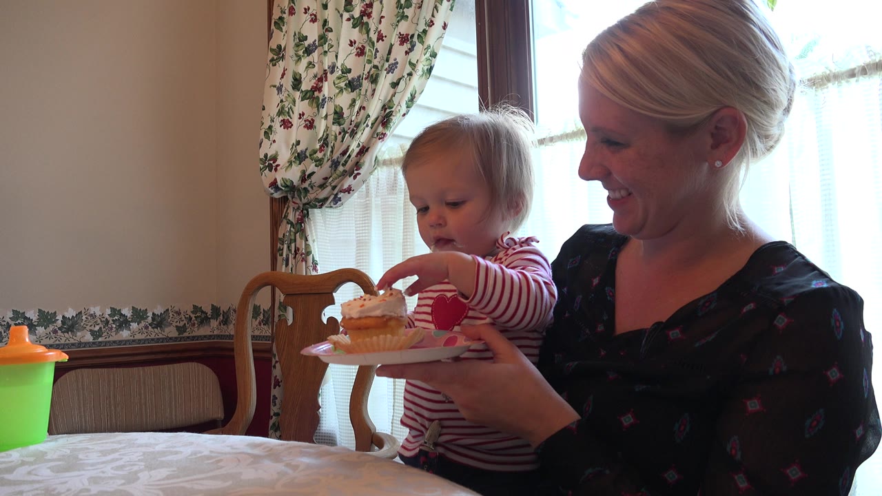 Mother holds a cupcake plate while a young child reaches toward the frosting.