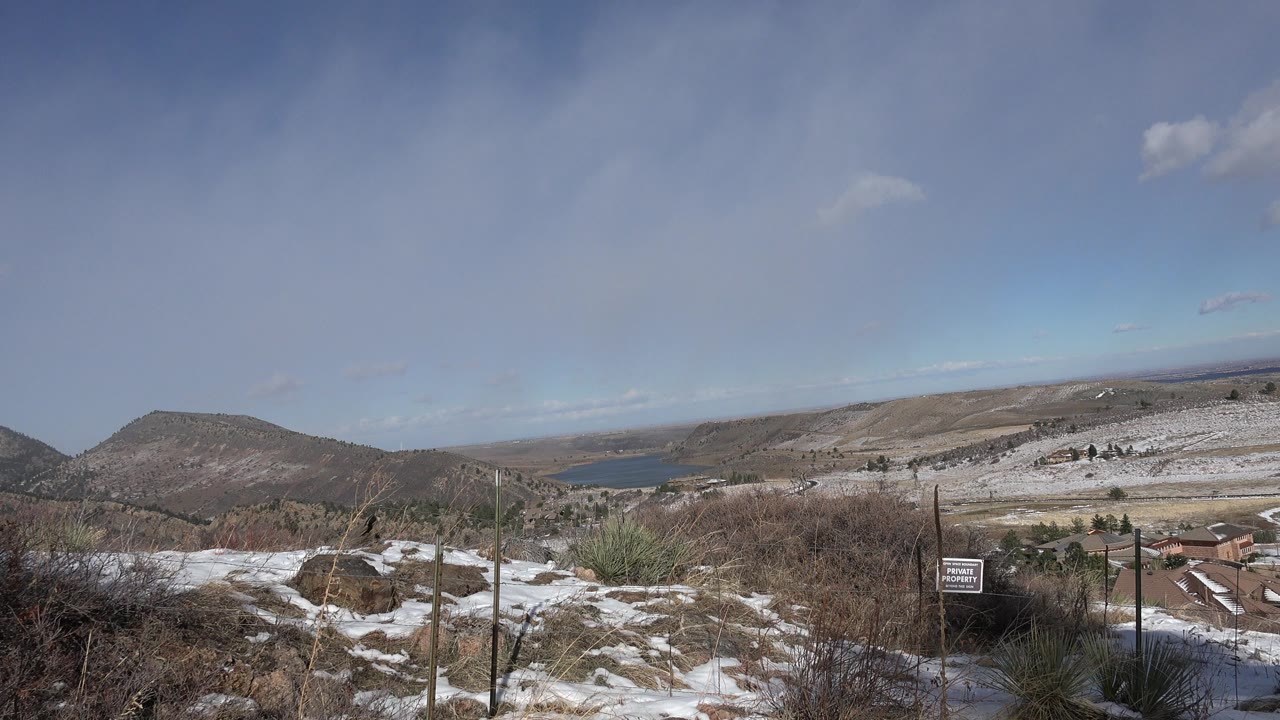 Snowy scrubland overlooking hills and a distant lake