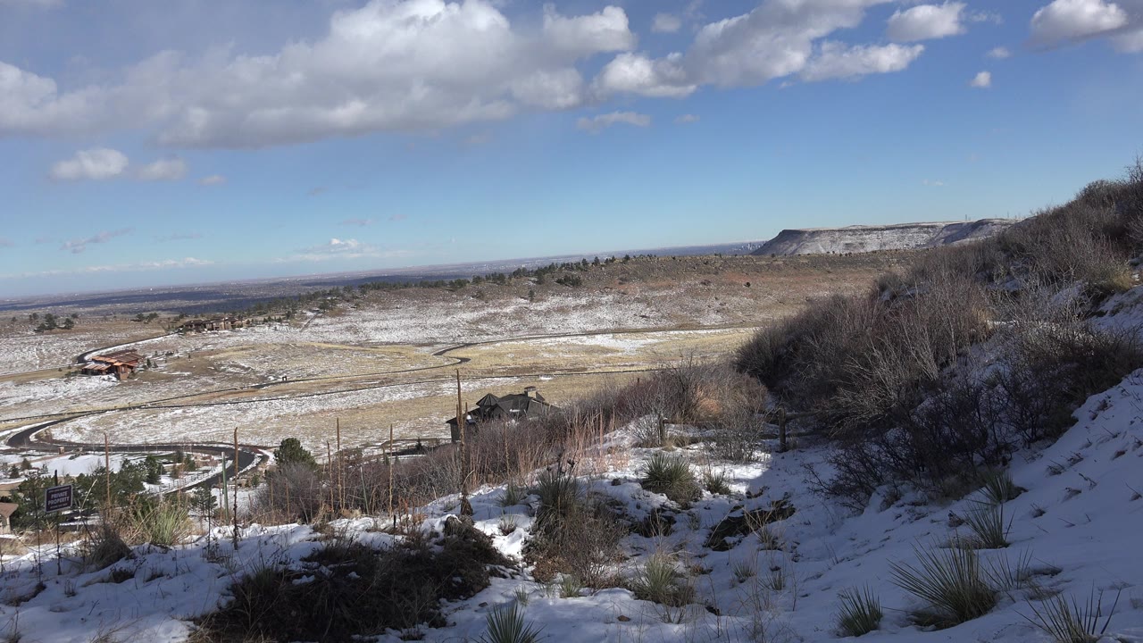 Snowy hillside overlooking a valley under blue sky and clouds.