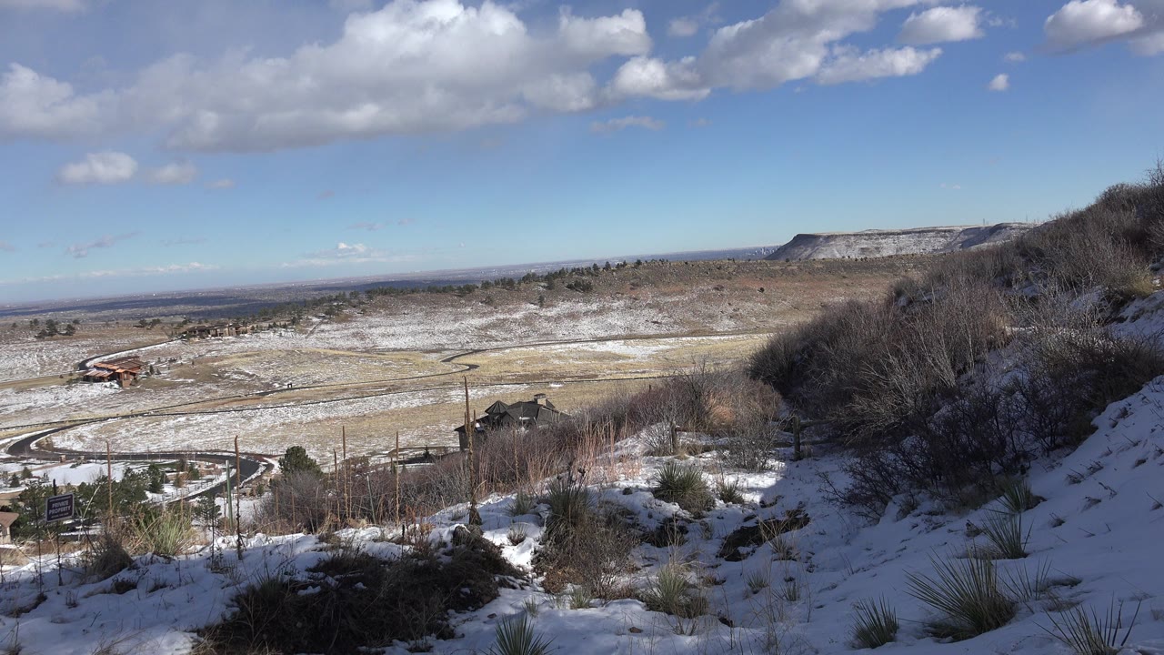 Snowy hillside overlooking a broad valley and distant ridge under blue sky