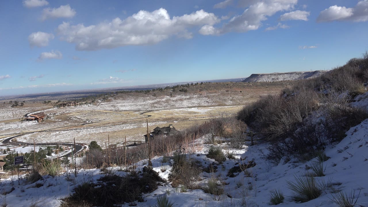 Wide winter view from a snowy hillside in Golden, Colorado, looking over open fields, a winding road, distant hills, and no visible people.