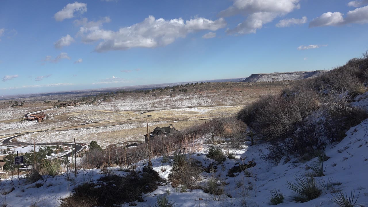 Snowy hillside overlooking a valley under a blue sky.