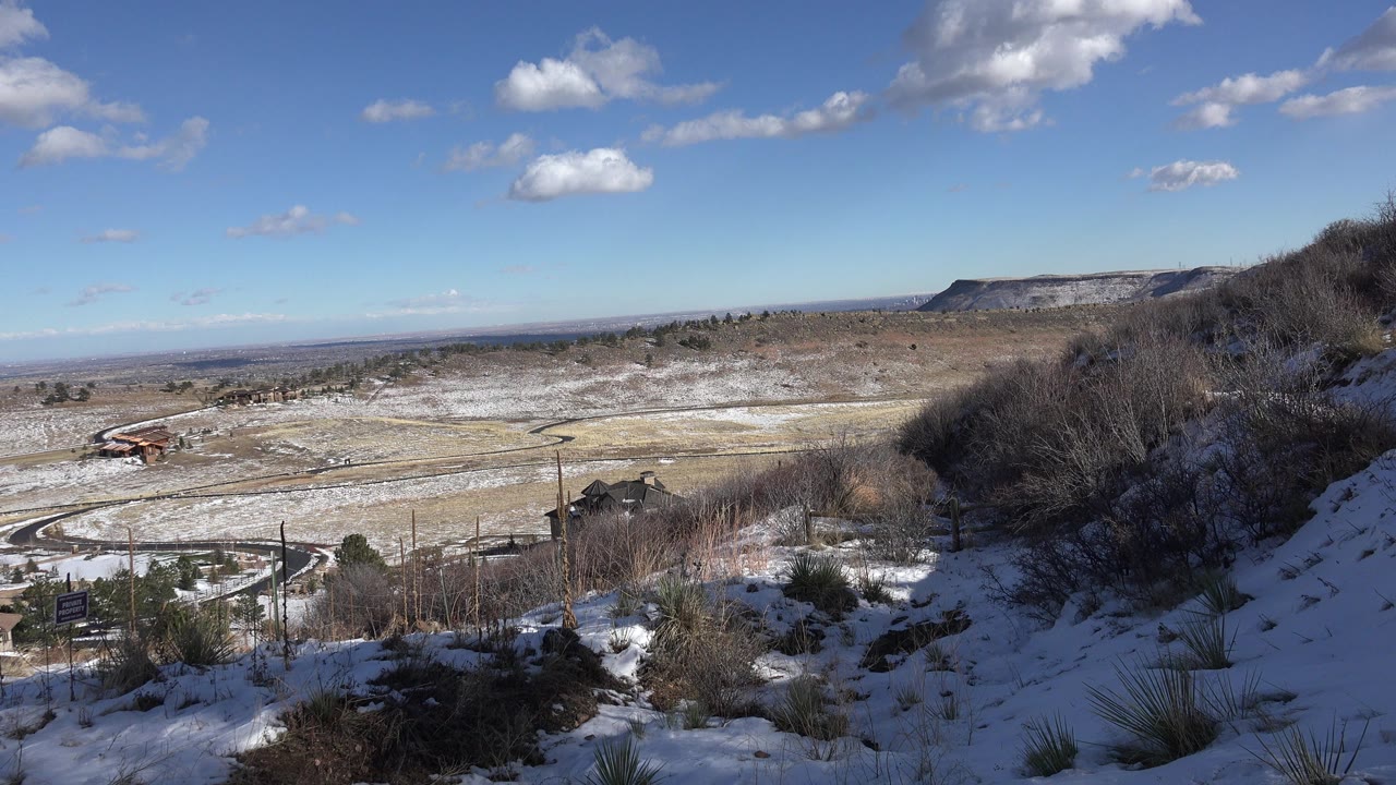 Snowy hillside overlooking a winding road and distant ridge under blue sky.