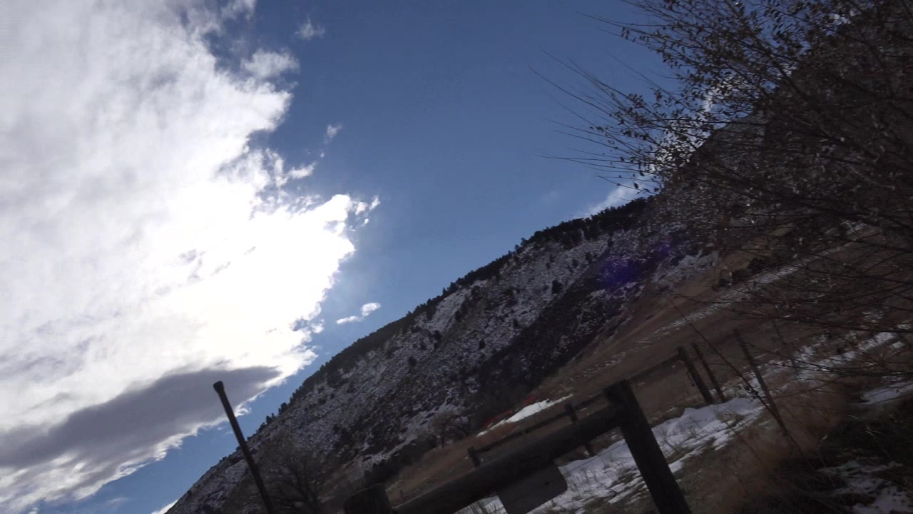 Cloudy mountain sky above a fence and snowy ground.