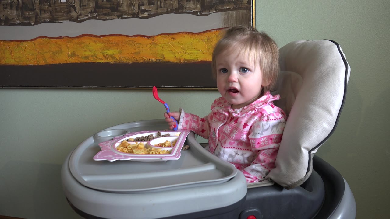 Child faces the camera from the high chair with fork lifted.