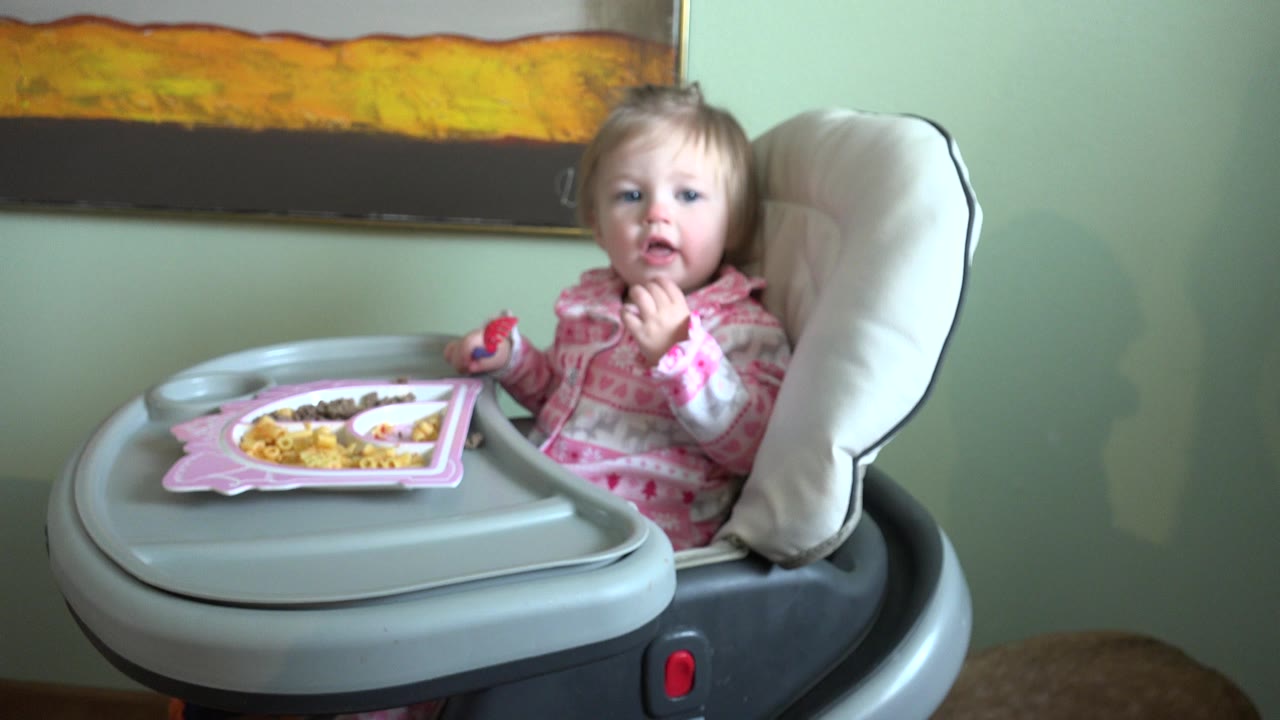 The child remains centered in the highchair in Westminster, Colorado, holding food near their mouth with a divided tray visible in front.