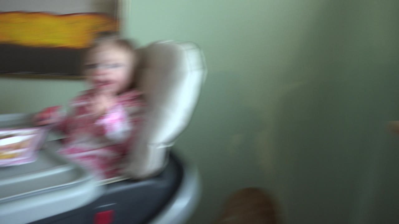Blurred baby in highchair as the camera shifts away.