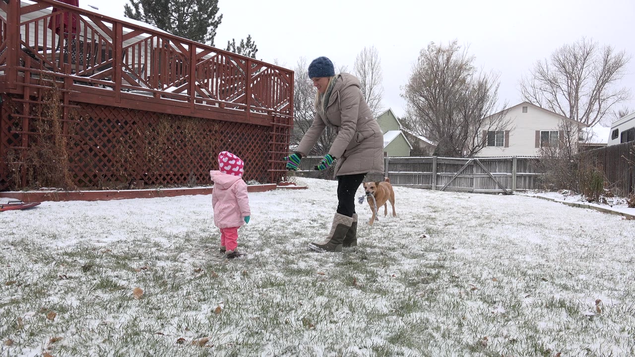 Adult and small child standing in a snowy backyard with a dog nearby.