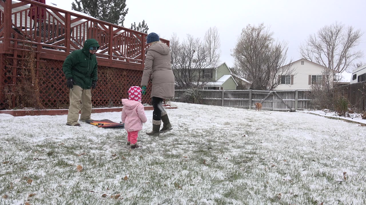 In Westminster, Colorado, the toddler stands closer to the adults as one person in a green hood leans toward the ground and another in a gray coat stands beside the red deck.