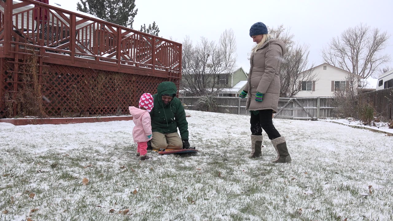 Child and two adults in a snowy backyard near a deck.