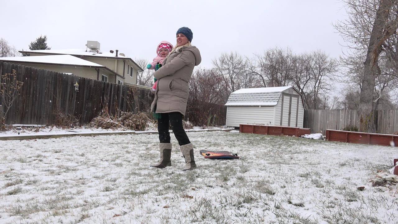 Adult holding a child in a snowy backyard.