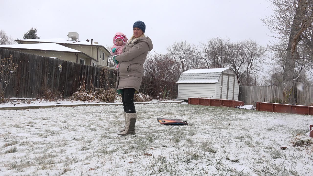 Woman holding a child in a snowy backyard.
