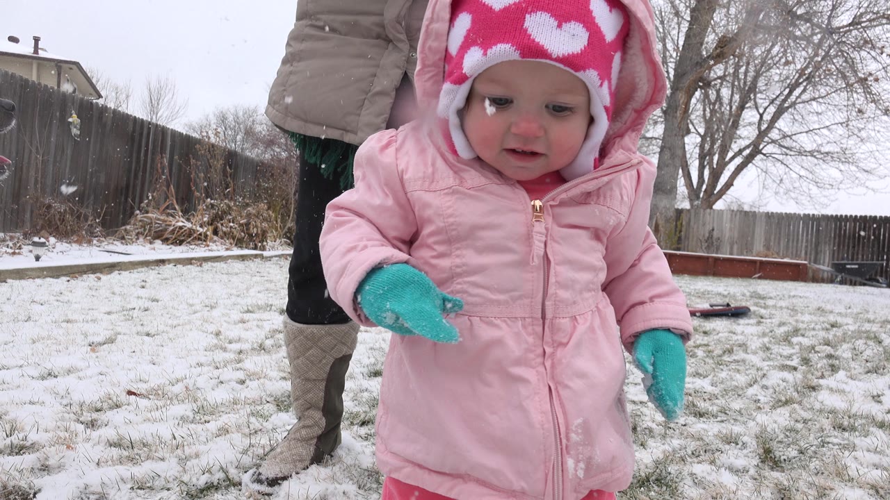 Close view of a toddler in a pink coat walking through snow.