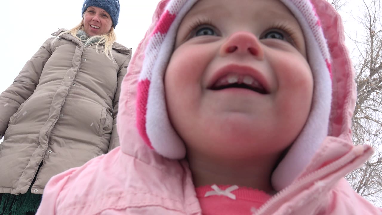 The toddler's face fills more of the Westminster winter frame, with the woman still visible behind and bare tree branches against a pale sky.
